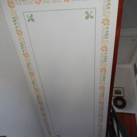 Weiße Dachluke mit umlaufender floraler Rahmenbemalung in Orange und Grün
